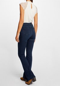 Mørkeblå vidde jeans med mellemhøj talje, kombineret med en cremefarvet top med blonder og små korte ærmer samt en nøglehul-detalje bagpå.