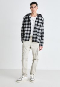 Black and white plaid flannel shirt with a hood, paired with beige cargo pants and grey and white sneakers. Casual fit, minimal detailing.