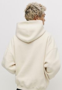 Felpa oversize color crema con cappuccio regolabile, spalle basse e polsini a coste. Tessuto morbido e design minimalista.