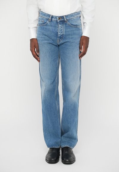 Jean en denim bleu clair avec une coupe droite, comportant cinq poches, des passants de ceinture et un léger décoloration. Associé à des chaussures en cuir noires.