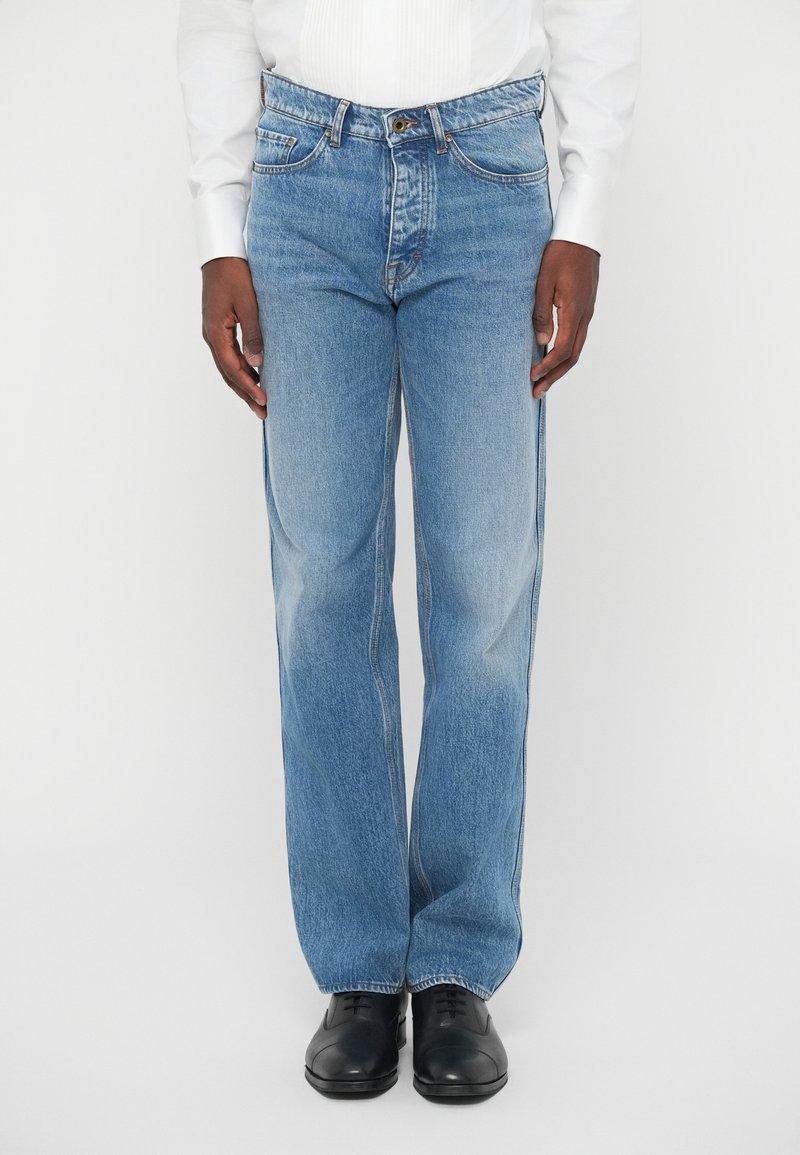 Svetlo modri jeansi iz denima s ravnim krojem, vsebujejo pet žepov, zankice za pas in subtilno zbledelost. V kombinaciji z črnimi usnjenimi čevlji.