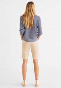 Sweter z dzianiny w jasnoniebieskim kolorze z teksturowanym wzorem, zestawiony z beżowymi szortami. Modelka w białych ankle boots. Widok z tyłu.