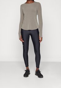 Dlouhý rukáv, světle šedý top s kulatým výstřihem, spárovaný s přiléhavými černými legínami. Modelka má na sobě černé sportovní boty. Hladká textura.