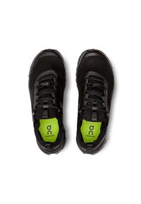 Chaussures de sport noires avec une tige en mesh, des détails texturés, des lacets noirs et une semelle intérieure verte vif arborant un logo.