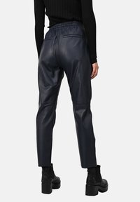 Pantalons en cuir bleu marine avec une coupe décontractée, taille élastique et poches arrière. Surface texturée avec une finition lisse. Associés à des bottines noires.