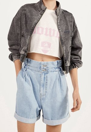 Person wearing a cropped black denim jacket, white cropped graphic t-shirt, and high-waisted light blue denim shorts with rolled hems.