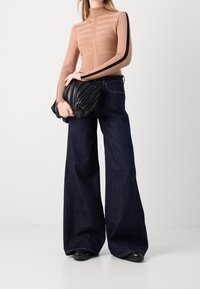 Suéter de cuello alto de manga larga en tono beige, con textura de rayas horizontales y una franja lateral negra, combinado con pantalones vaqueros oscuros de pierna ancha y un bolso negro con fruncido.