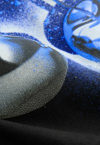 Close-up van een textuurdoekprint met driedimensionale blauwe en grijze cirkelvormige vormen met een gestippeld, verheven oppervlak op een zwarte achtergrond.