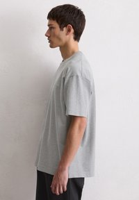 Szara koszulka krótki rękaw w luźnym kroju, okrągły dekolt, wykonana z miękkiej bawełny, z minimalnym szyciem i bez widocznych logo.