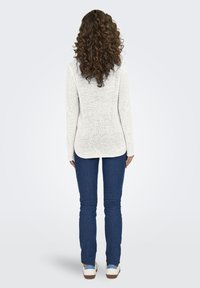 Maglione bianco a maglia con trama, maniche lunghe, abbinato a jeans skinny blu e scarpe bianche casual, visto di spalle.