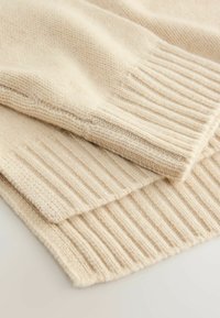 Beige gestrickter Pullover mit gerippten Bündchen und Saum. Die weiche Textur, das Zopfmuster und das leicht voluminöse Design verleihen ihm ein gemütliches Aussehen.