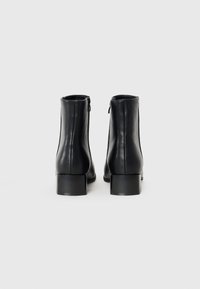 Botines de cuero negro con una textura suave, cierre de cremallera en la parte trasera y diseño de tacón cuadrado.