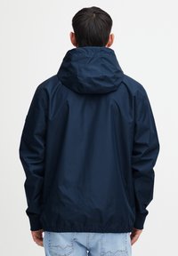 Laivaston tuulenpitävä takki hupulla, joustavilla hihansuilla ja vyötäröllä; sileä, kevyt kangas; takanäkymä, jossa on vähäiset suunnittelutiedot.