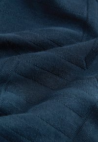 Țesătură tricotată de culoare albastru închis, cu un model diagonal texturat, având șanțuri subtile și tehnici de cusătură variate, care creează o adâncime vizuală.