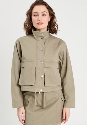 Chaqueta corta color caqui hecha de tela de algodón con un cuello alto, botones de presión y dos bolsillos frontales. Cuerda ajustable en el dobladillo inferior.