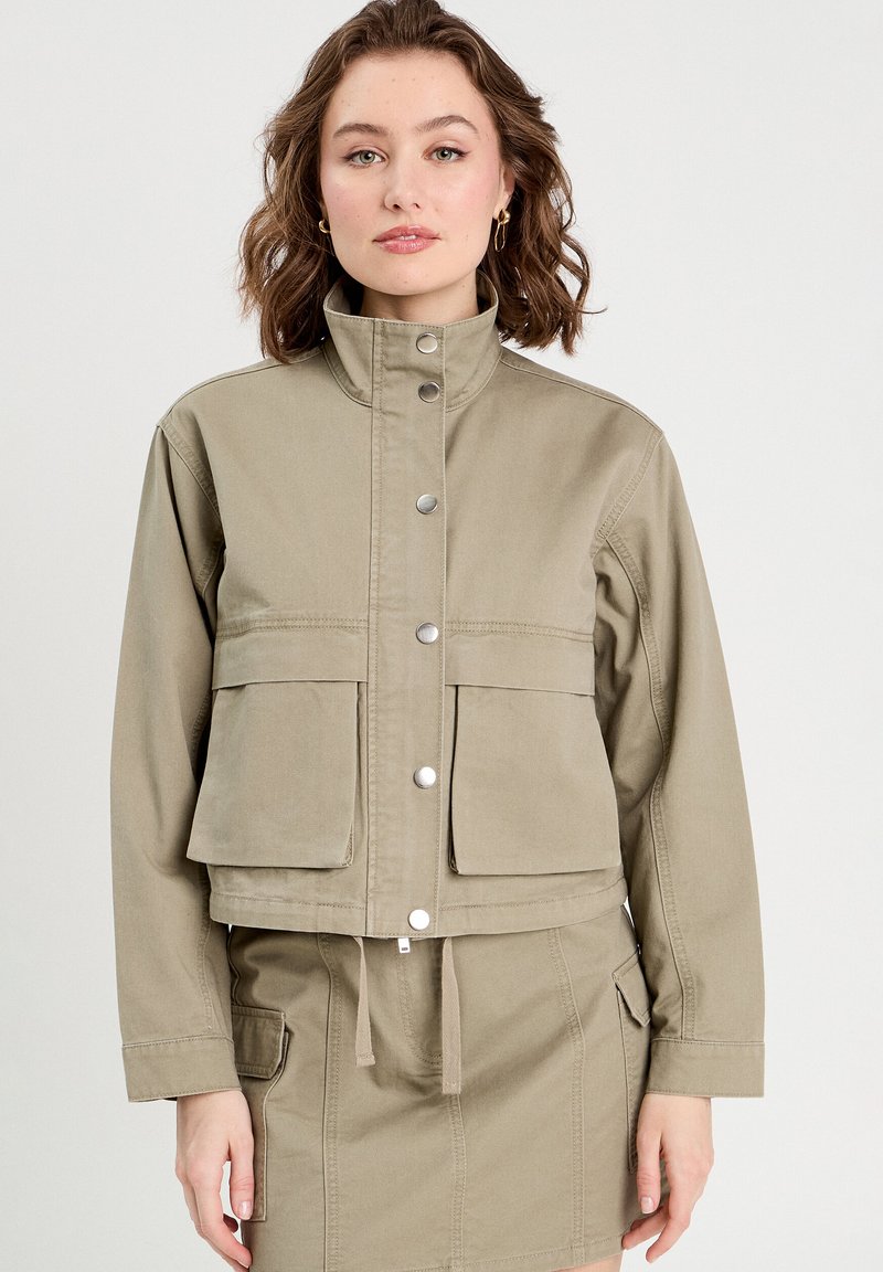 Veste cropped en khaki en tissu de coton avec un col haut, des boutons-pression et deux poches avant. Cordon de serrage à l'ourlet inférieur.