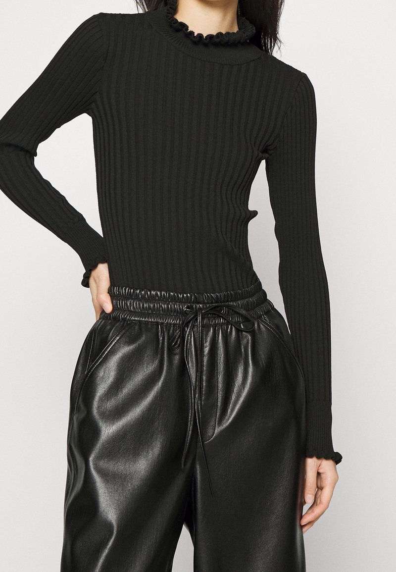 Haut noir à manches longues côtelé avec un col montant froncé, associé à un pantalon noir brillant à taille élastique avec cordon de serrage.