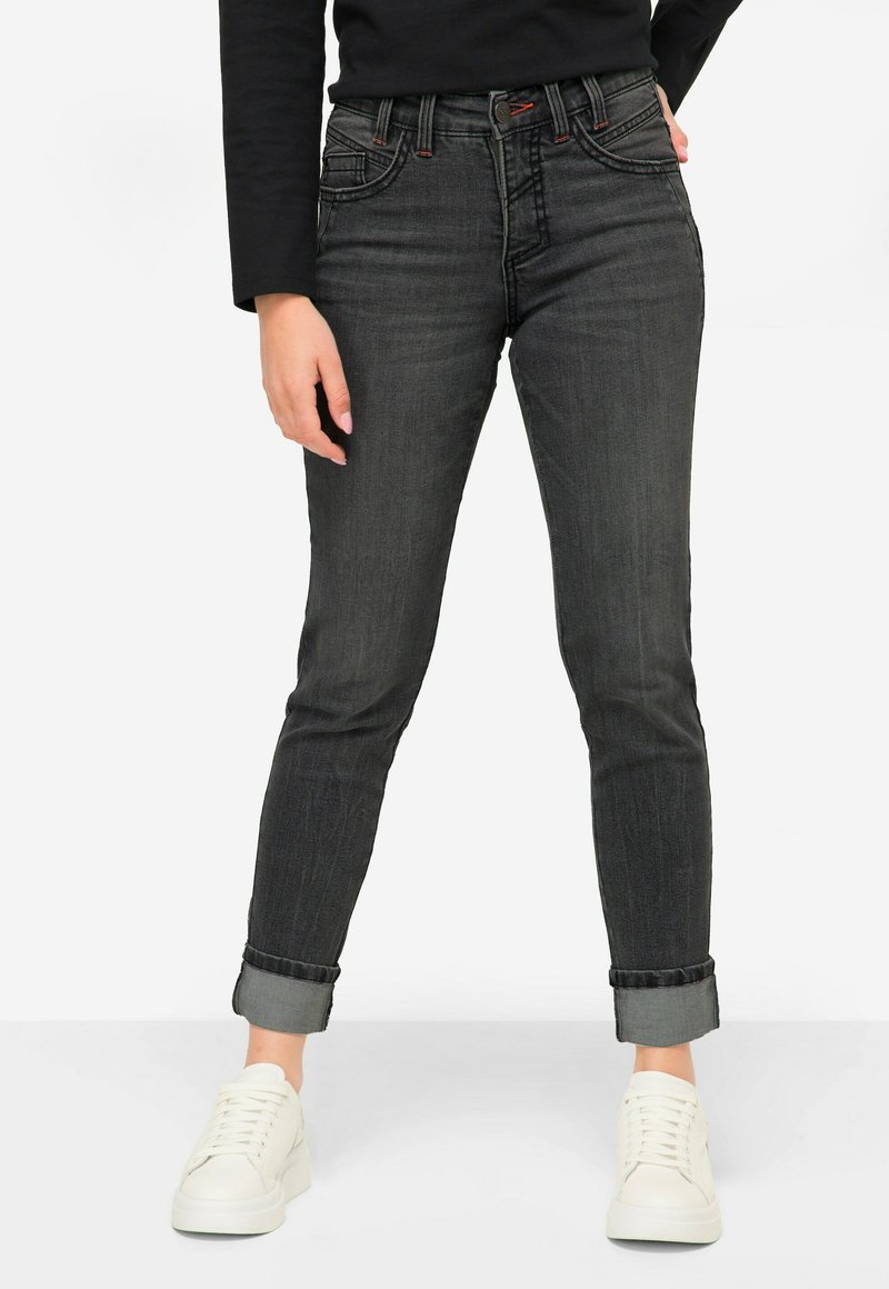 Jean oscuro con un ajuste Slim y puños enrollados, con costuras en contraste y cinco bolsillos. Combinado con zapatillas blancas.