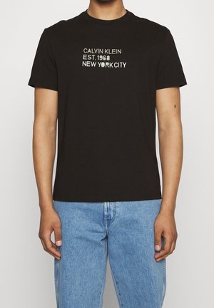 Czarna bawełniana koszulka z krótkim rękawem, z białym napisem: "CALVIN KLEIN EST. 1968 NEW YORK CITY" na przodzie. Dopasowany krój.