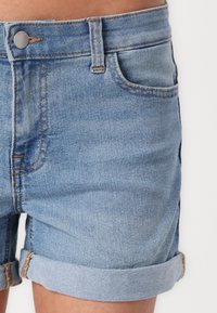 Ljusblå denimshorts med uppvikta nederkanter, femfickdesign och kontrasterande orange sömmar, med knappstängning i metall.
