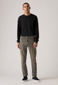 Black long-sleeve shirt, faded green jeans, and black sneakers. The shirt has a ribbed texture; jeans feature classic five-pocket design.