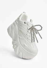 Vit sneaker med texturerat material, kraftig sula och förhöjda mönster. Utrustad med silverfärgade snören och en förlängd häl-design.