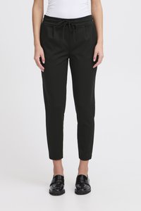 Fekete, enyhén szűkülő nadrág rugalmas derékpánttal és húzózsinórral, elöl behúzásos részletekkel és sima tapintású anyagból. Fényes fekete cipővel viselve.