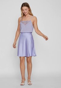 Φόρεμα λιλά με εφαρμοστό μπούστο, δαντελένιες λεπτομέρειες και φούστα από σατέν με φουσκωτό τελείωμα. Διαθέτει λεπτές τιράντες και λείο φινίρισμα.