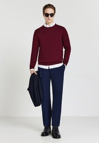 Bordeauxfarbiger Pullover, weißes Hemd mit Kragen, marineblaue Hose und schwarze Stiefel, accessoriert mit schwarzen Sonnenbrillen, minimalistisches Design.