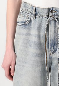 Light blue denim pants with a loose fit, featuring a drawstring waist, two front pockets, and contrasting stitching details.