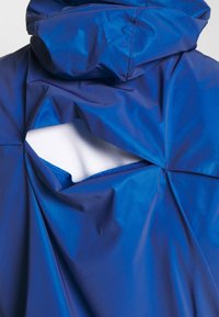 Blue, waterproof jacket featuring a large hood and an open back design revealing white fabric. Smooth texture with stitched detailing.