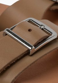 Tan leather sandal strap with a silver metal buckle. The strap features a smooth texture and a minimalist design, securing with a single hole.