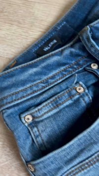 Sinised teksad, kokku volditud, näidates esitaskuid, metallnööpe ja must rõivamärk valge tekstiga vöörihma sees.