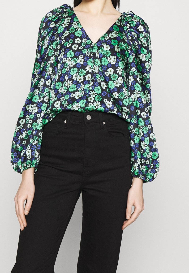 Kwiatowa bluzka z głębokim dekoltem w kształcie litery V, bufiastymi rękawami, zielono-białymi kwiatami na granatowym tle, połączona z czarnymi, wysokim pasem dżinsami.