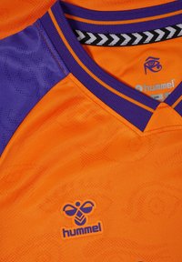 Orange och lila sporttröja med ett strukturerat mönster, med en svart och vit chevron-halsringning och en blå "hummel"-logotyp.