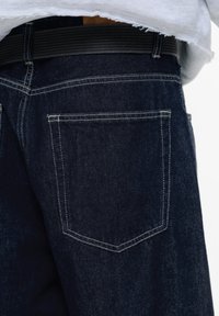 Mörka denimjeans med en enda bakficka, synlig sömnad och ett svart bälte. Tyget har en slät textur och är något slitet.