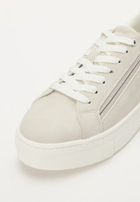 Sneakers grigio chiaro in suede con lacci bianchi, dotati di una suola in gomma testurizzata e un dettaglio zip decorativo di lato.