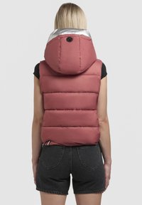 Vesta căptușită în roz pal cu o glugă argintie. Are cusături orizontale și un accent de metal rotund la gât. Purtați-o peste pantaloni scurți negri.