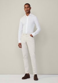 Witte button-up shirt gecombineerd met crèmekleurige broek en bruine nette schoenen, met een getailleerd ontwerp, lange mouwen en knopen.