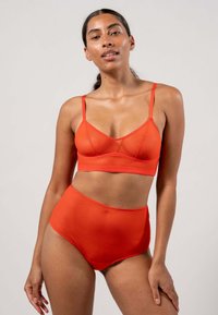 Röd underklädesset bestående av en mjuk, slät bralette med justerbara remmar och matchande högmidjade trosor, båda med en sömlös design.