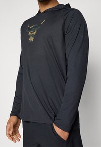 Langärmliger Kapuzenpullover in Dunkelblau mit einer strukturierten Grafik eines Bullen-Schädels in Grün und Gold auf der Vorderseite; bietet eine lockere Passform und ein leichtes Material.
