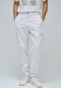 Pantalones cargo blancos con bolsillos laterales, hechos de una tela ligera. Combinados con zapatillas blancas, que tienen una textura suave y un ligero brillo.