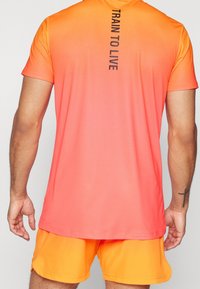 Camiseta de manga corta en degradado de color naranja brillante, con el texto "ENTRENAR PARA VIVIR" impreso verticalmente en negro en la parte posterior.