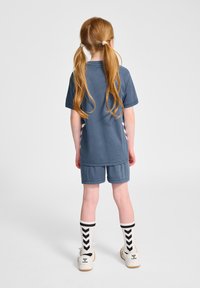 Niebieski komplet sportowy składający się z krótkiego topu i spodenek, z czarno-białymi paskowanymi skarpetkami i jasnymi butami. Miękka tkanina, casualowy design.