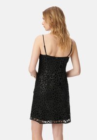 Abito in pizzo nero con un motivo a fiori ritagliato, spalline sottili e orlo fino al ginocchio. Fodera interna liscia visibile attraverso i ritagli.