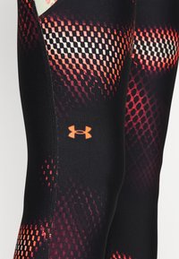Czarne legginsy sportowe z teksturowanym wzorem w odcieniach czerwieni i pomarańczu, z logo Under Armour w kolorze pomarańczowym na dolnej części nogawki.