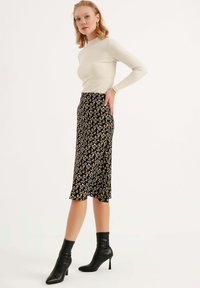 Zwarte bloemen midi rok van luchtige stof, met kleine witte en oranje bloemen, gecombineerd met een crème lange mouw top en zwarte hoge enkel laarzen.