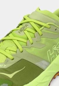 Πράσινο αθλητικό παπούτσι με διχτυωτό και συνθετικό υλικό, υφασμένη επιφάνεια, κορδόνια και λογότυπο HOKA. Περιλαμβάνει αντανακλαστικές λεπτομέρειες.