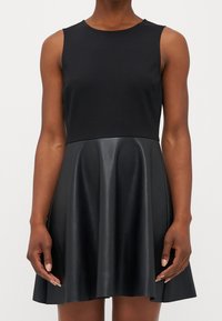 Černé šaty s upnutým bezramínkovým topem z hladké látky, přecházející do rozšířené sukně vyrobené z lesklé umělé kůže.