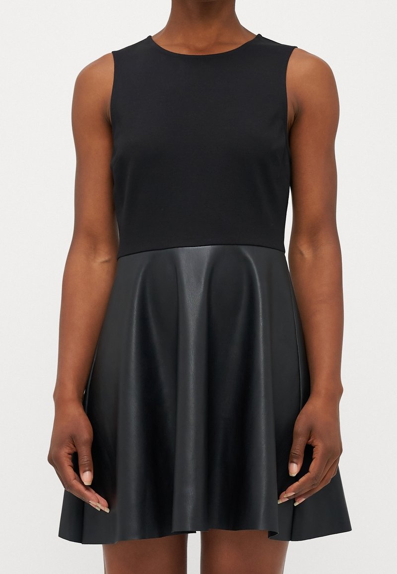 Černé šaty s upnutým bezramínkovým topem z hladké látky, přecházející do rozšířené sukně vyrobené z lesklé umělé kůže.